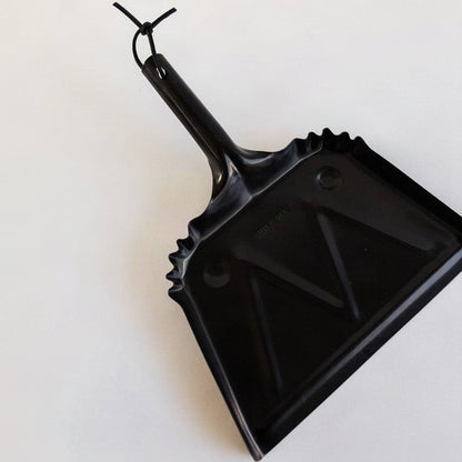 Angled view of the black steel Farmhouse Dustpan with a leather hanging loop.