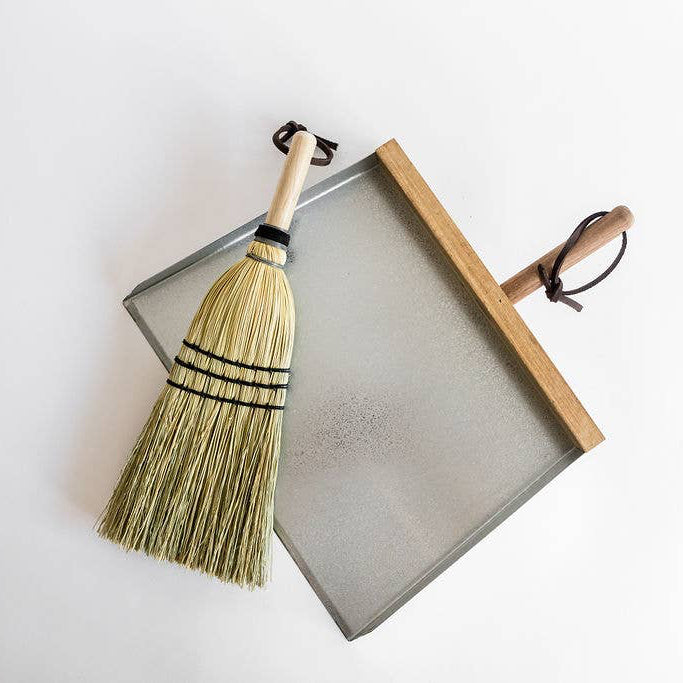 Natural hand broom resting over a dustpan, which is not included.