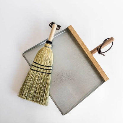 Natural hand broom resting over a dustpan, which is not included.