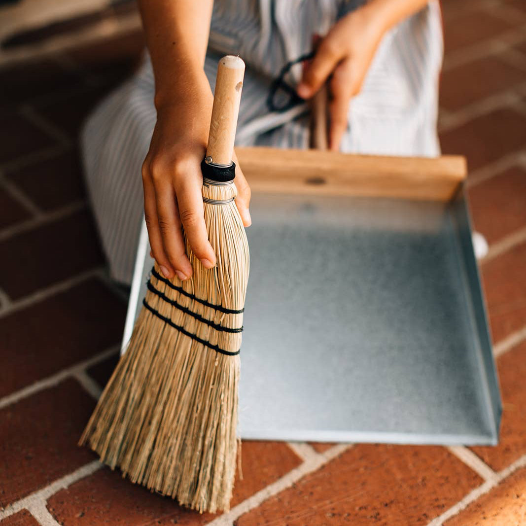 Natural hand broom in use beside a dustpan, which is not included.