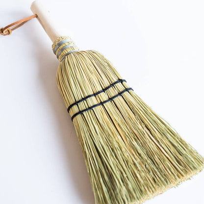 Natural hand broom with pale bristles, dark stitching and a wooden handle.