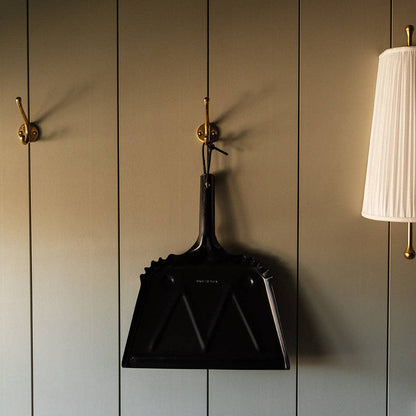 Black Farmhouse Dustpan hanging on a light paneled wall.