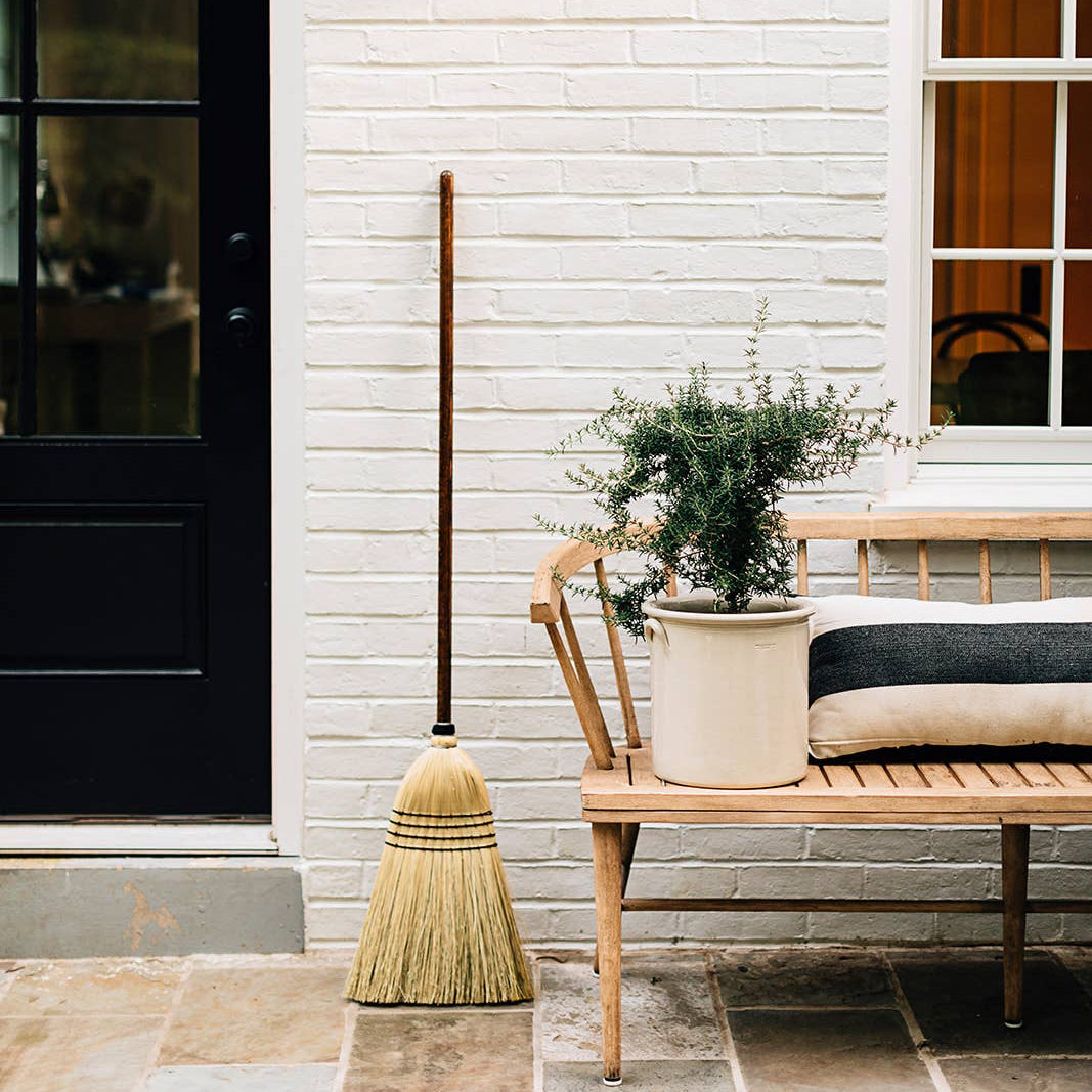 Natural broom leaning beside a bench on a porch.