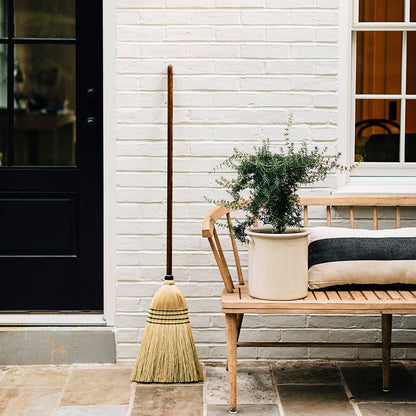 Natural broom leaning beside a bench on a porch.