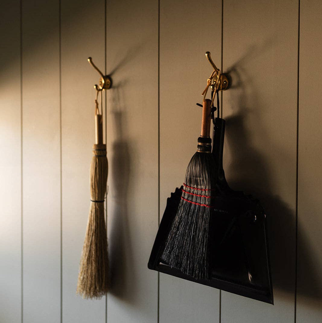 Black Farmhouse Dustpan hanging beside a hand broom above a woven basket.