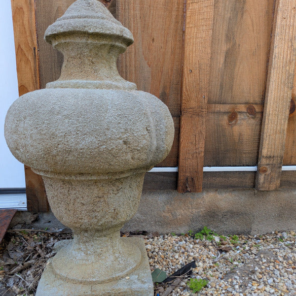One Valmont garden finial against a wood fence, showing its urn-shaped body and tapered base.