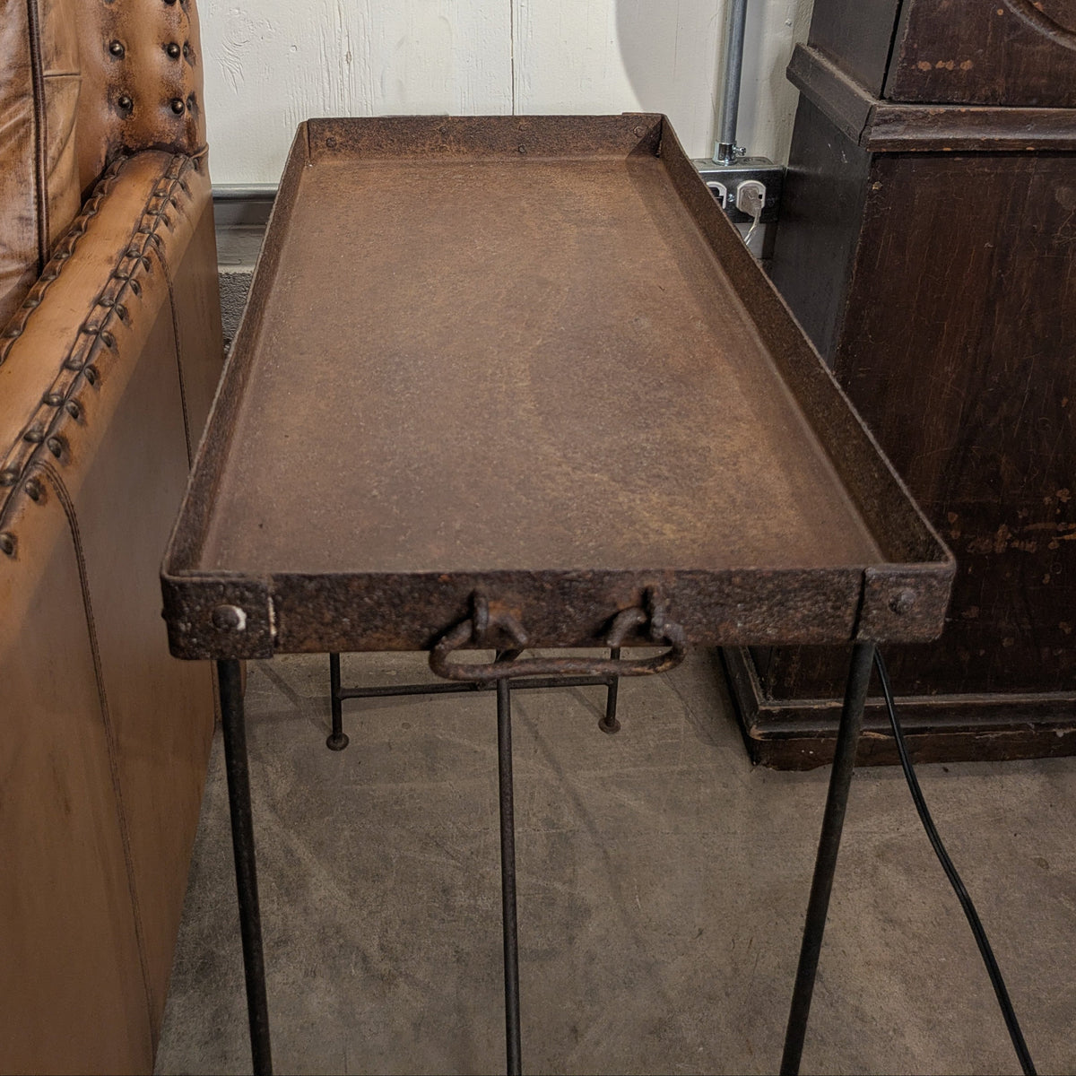 Metal tray table showing its shallow rectangular top, front handle and slender iron stand.